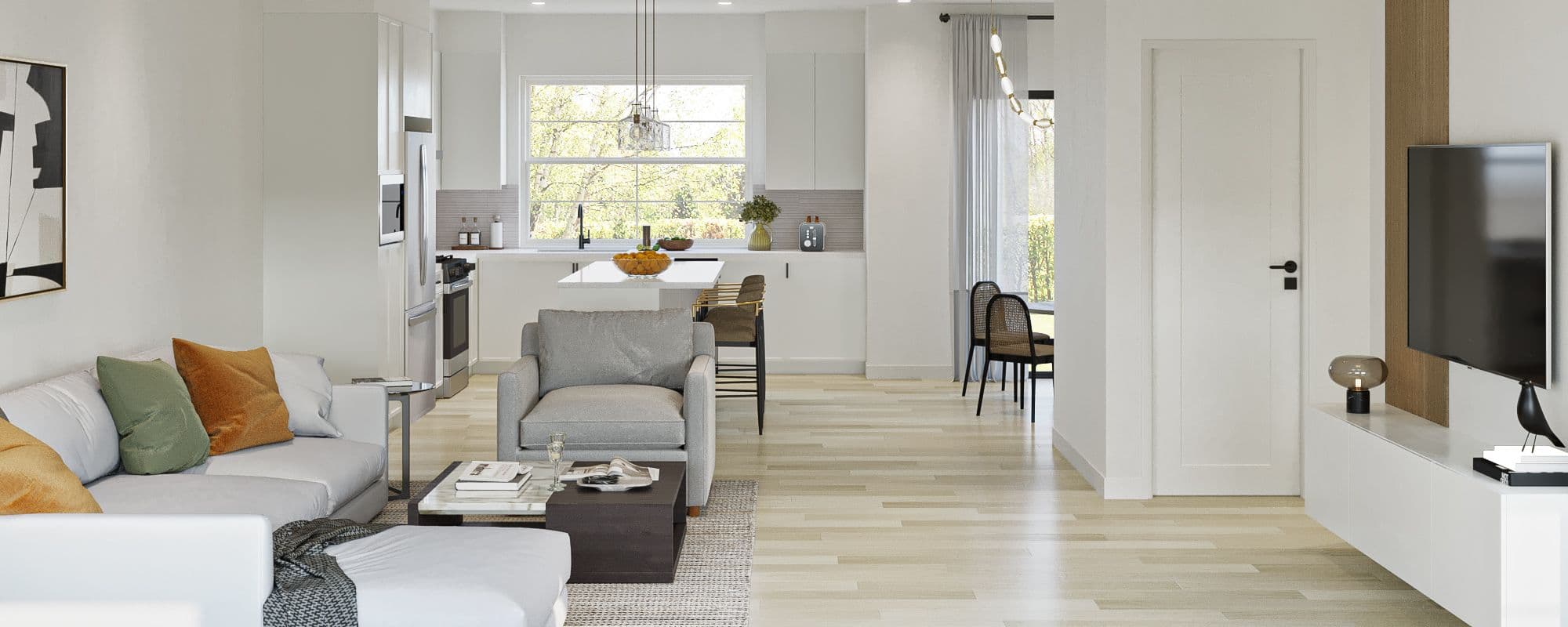 The Westminster – A bright, open-concept living and kitchen area featuring light hardwood floors and crisp white walls. The foreground showcases a comfortable living space with a sectional couch, armchair, and coffee table, while the background reveals an all-white kitchen with stainless steel appliances, an island with bar seating, and a large window bringing in natural daylight.