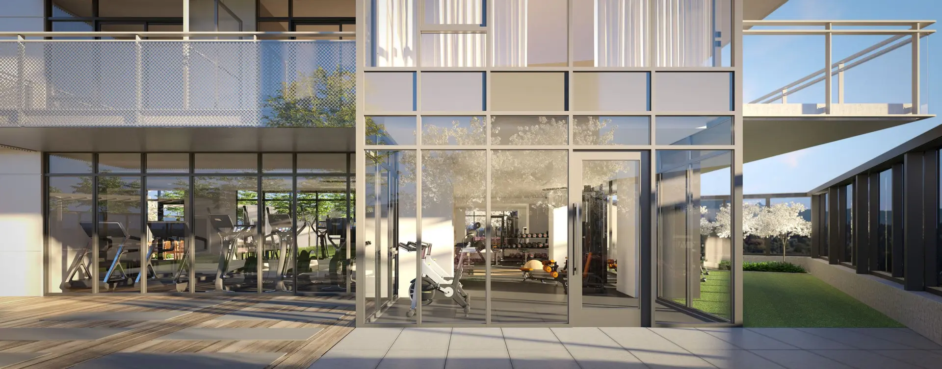 Elmwood – An outdoor terrace connects through floor-to-ceiling glass walls to a residential fitness center equipped with treadmills, stationary bikes, and free weights. Outside, the bright, sunlit deck features yoga mats laid out on wood planking adjacent to a tiled walkway and small lawn area.