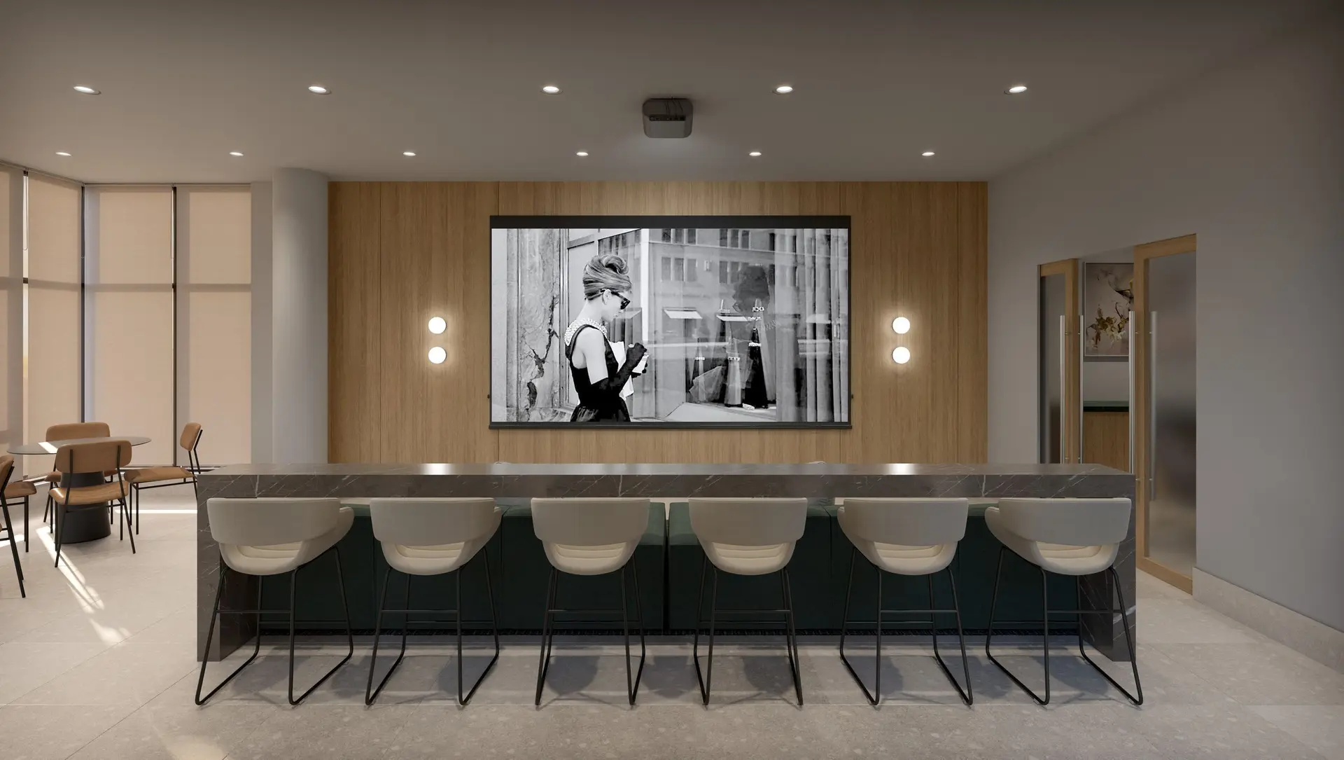 Elmwood – A contemporary screening or media lounge features a large projection screen mounted against a vertical wood-paneled accent wall, flanked by modern circular sconces. In the foreground, a long dark marble high-top table is lined with sleek beige barstools, set under warm recessed ceiling lighting.
