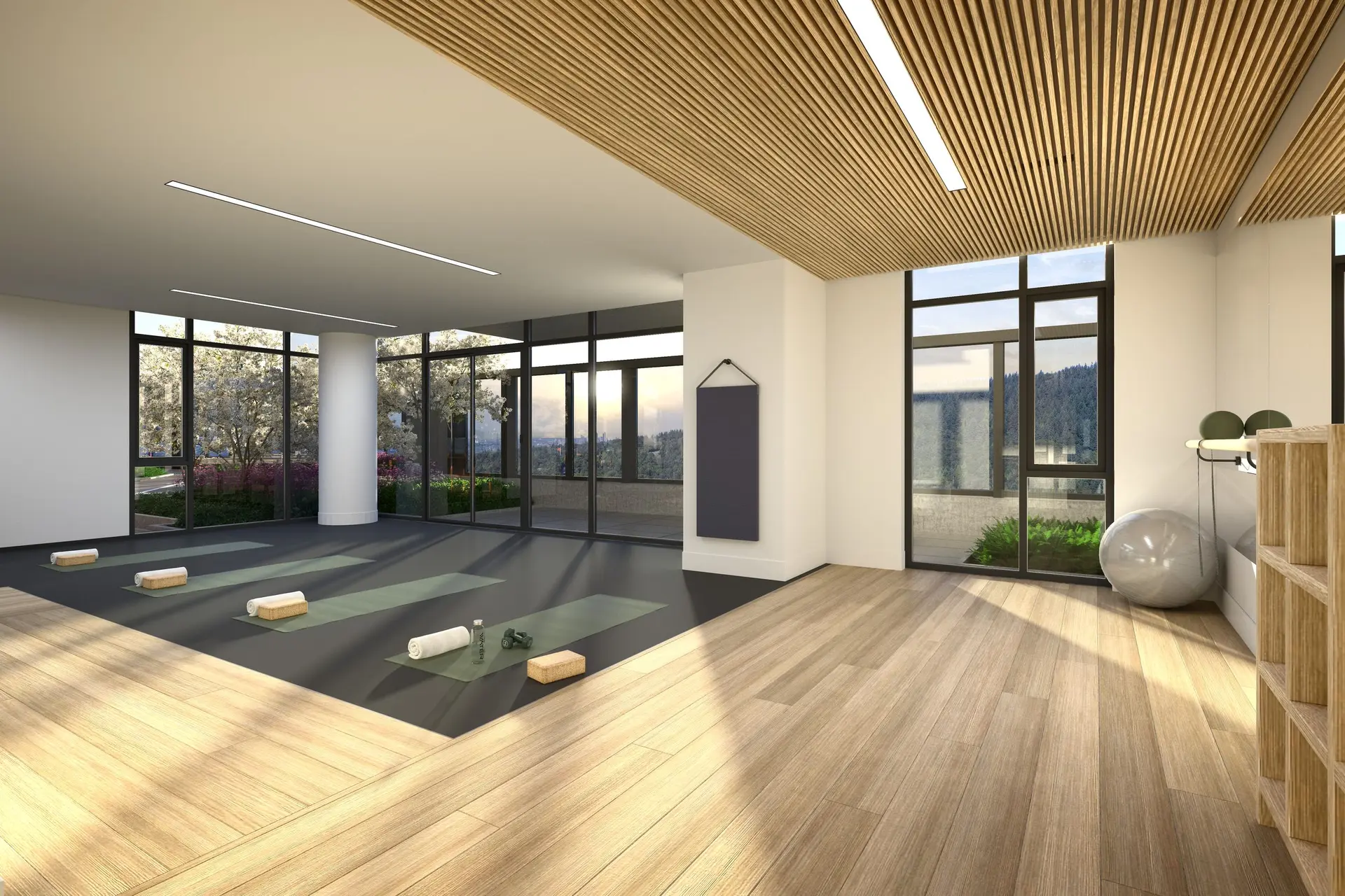 Elmwood – A bright yoga and fitness studio featuring light wood flooring, a slatted timber ceiling detail, and yoga mats set out on a dedicated workout area. Floor-to-ceiling windows fill the space with natural daylight and overlook outdoor landscaping and distant forested hills.