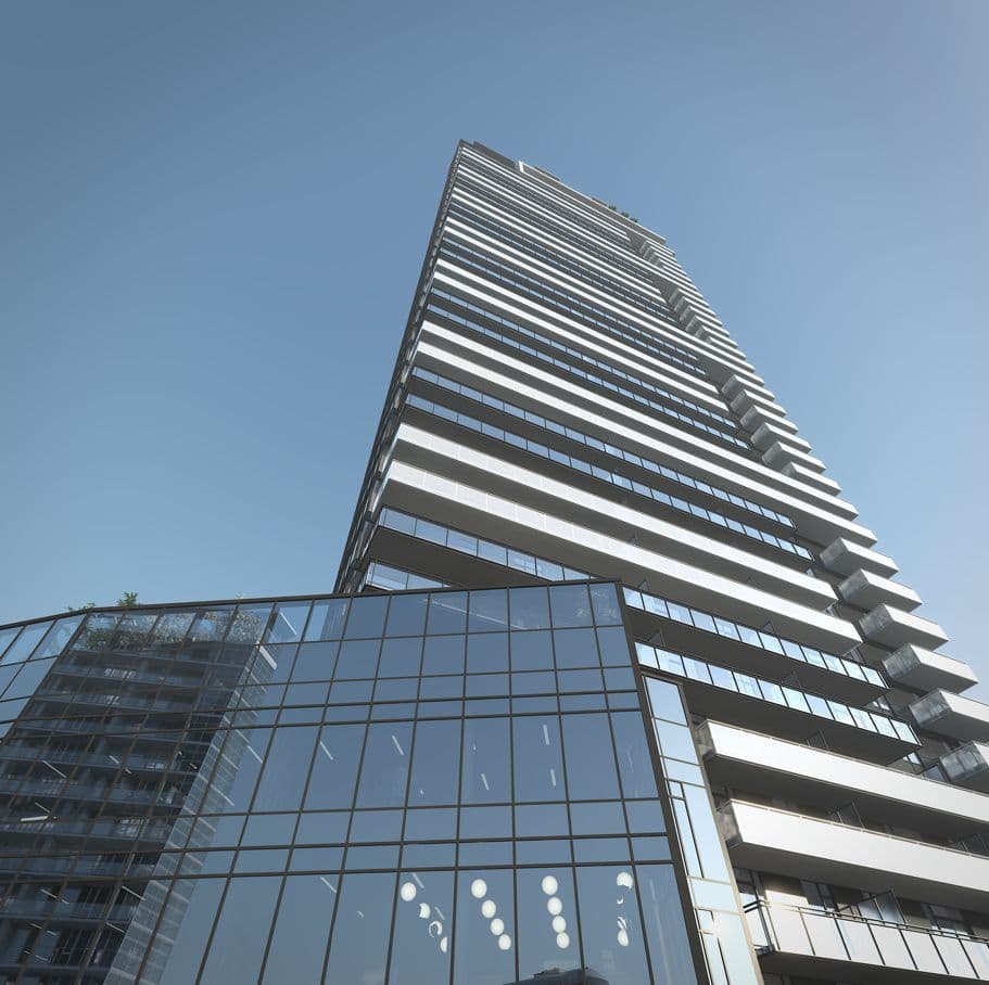 Elmwood – Upward angled view of a high-rise condo tower with stacked white balconies, seen from street level beside a glass podium building.