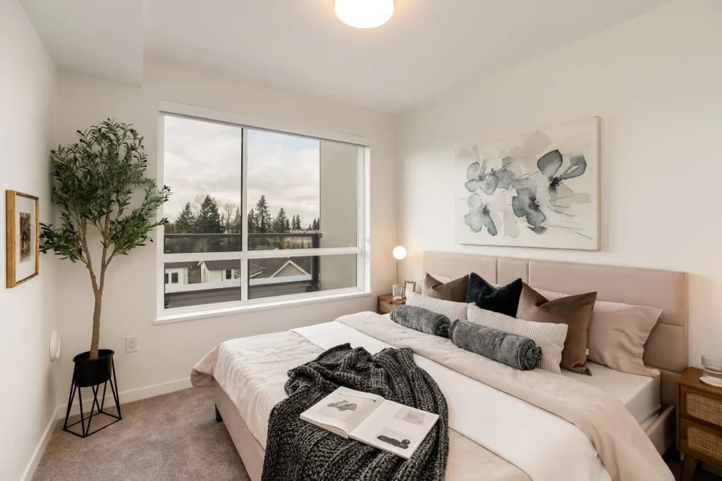 The Hive 2 – Bedroom with a king bed, patterned throw pillows, a potted tree, and a window looking out over neighboring rooftops and trees.