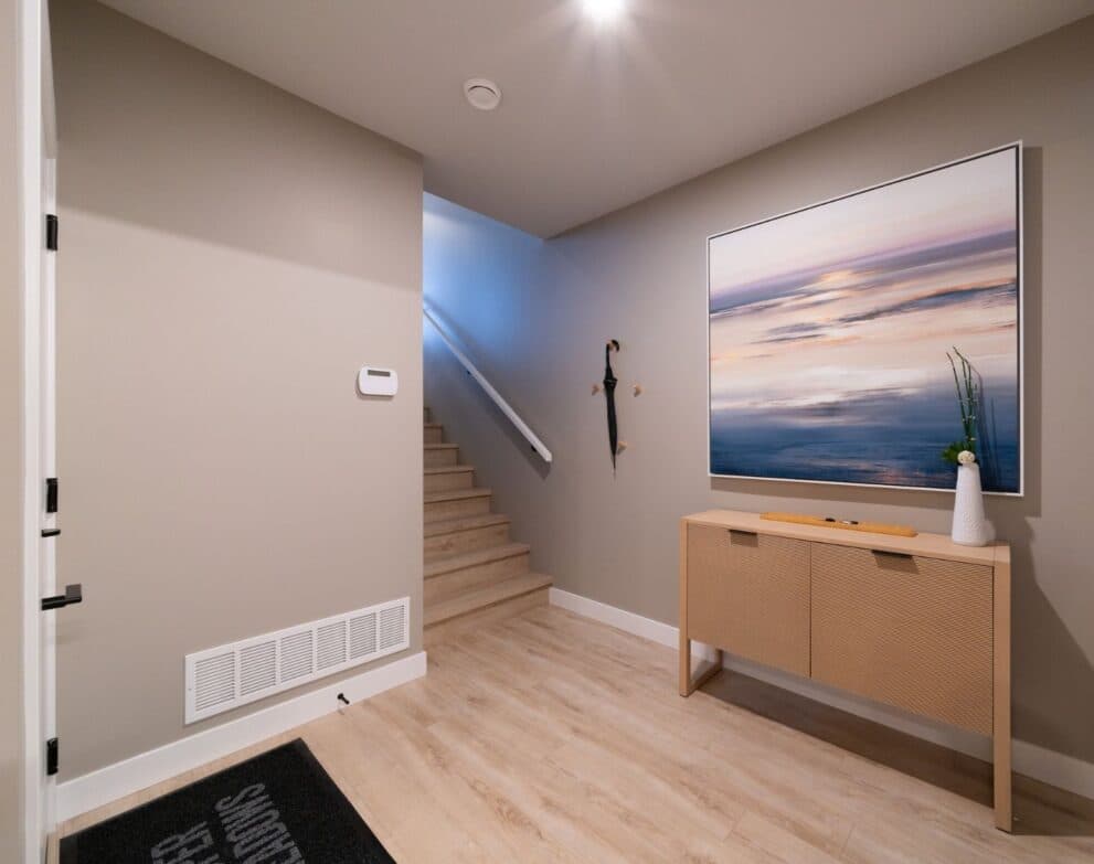South Hill – Entryway with a staircase, a wood console table, hooks for an umbrella, and a large framed seascape painting on the wall.