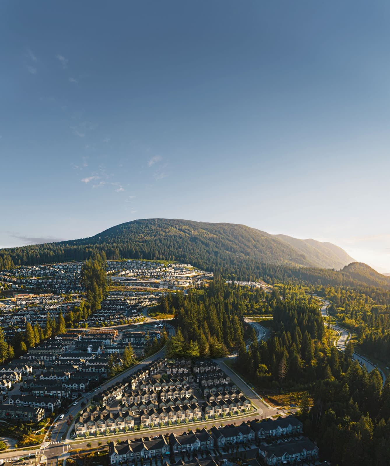 Culmena – Drone shot of a suburban townhouse neighborhood nestled among forested mountains at sunset.