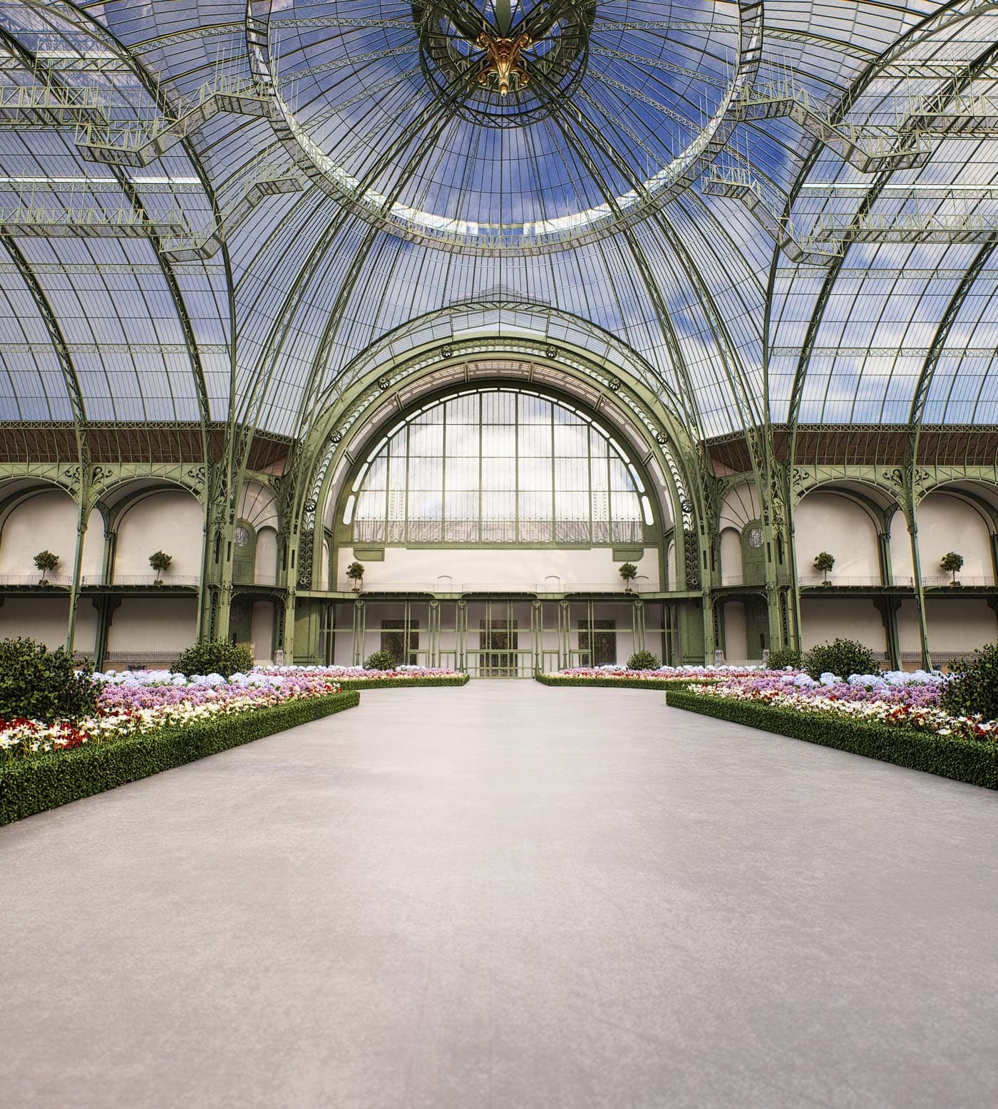 Greenhouse – A rendering of a grand glass-domed conservatory hall with ornate ironwork, manicured flower beds, and topiary trees along a wide walkway.