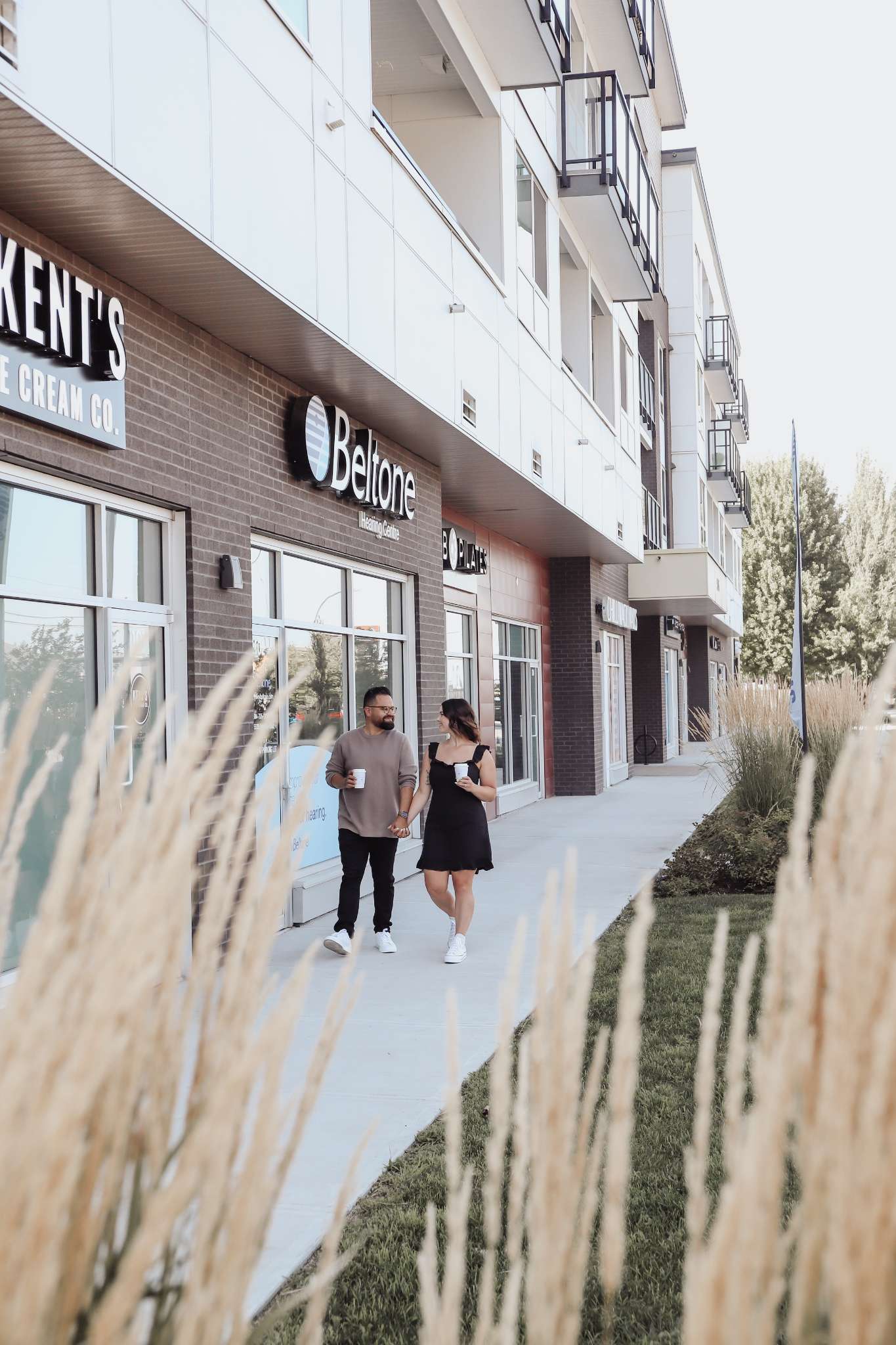 York Residences - Building C – Street-level view of the building's ground-floor retail units, including a Beltone hearing centre and ice cream shop, with a couple walking past holding coffee.