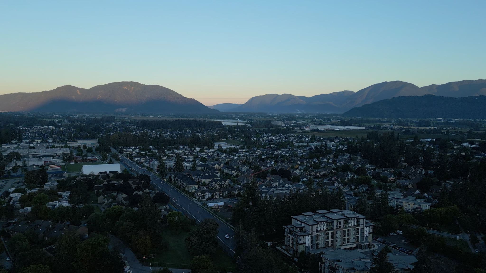 York Residences - Building C – A dusk aerial view over the surrounding neighbourhood and mountains, with the condo building visible in the foreground bottom right.