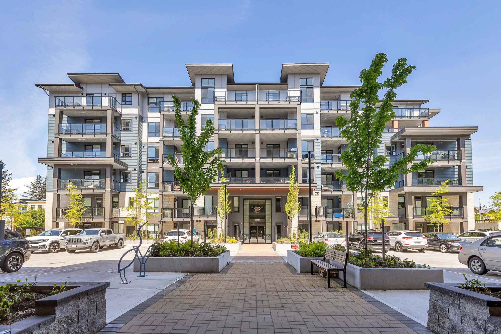 York Residences - Building C – Front entrance of the condo building with its main glass doors, address number 45497, landscaped planters, and parked cars.
