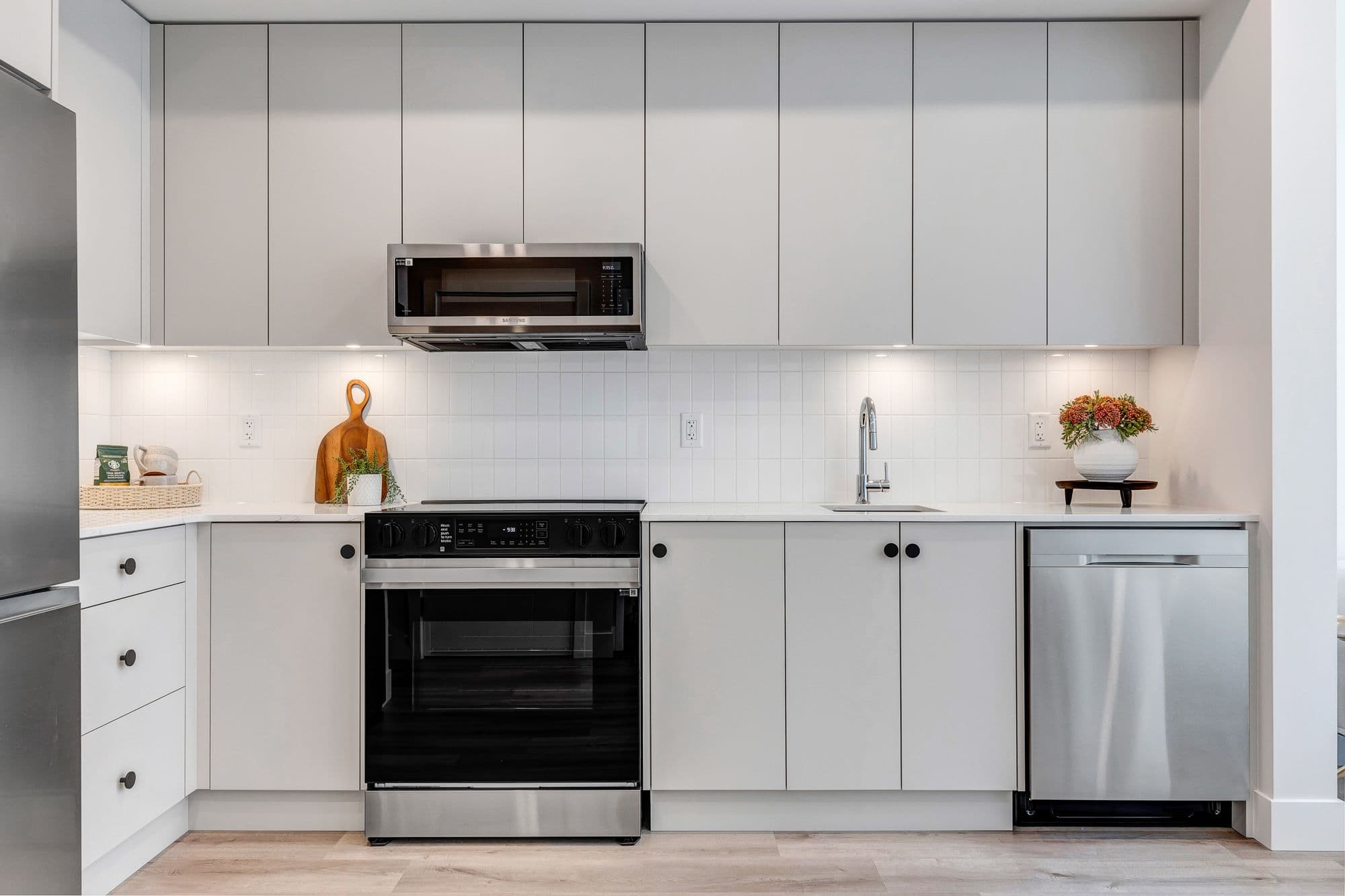 York Residences - Building C – A light grey kitchen with a stainless range, microwave, dishwasher, and refrigerator, viewed from an adjacent dining nook.