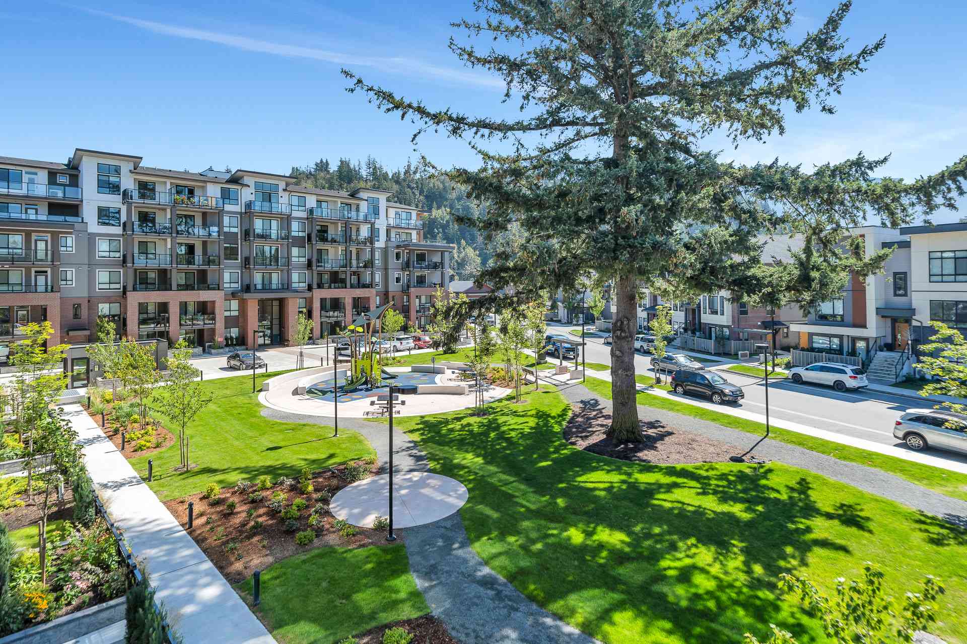 York Residences - Building C – An elevated view of a landscaped plaza with a children's playground, benches, and pathways in front of the condo building, with a street and other homes beyond.