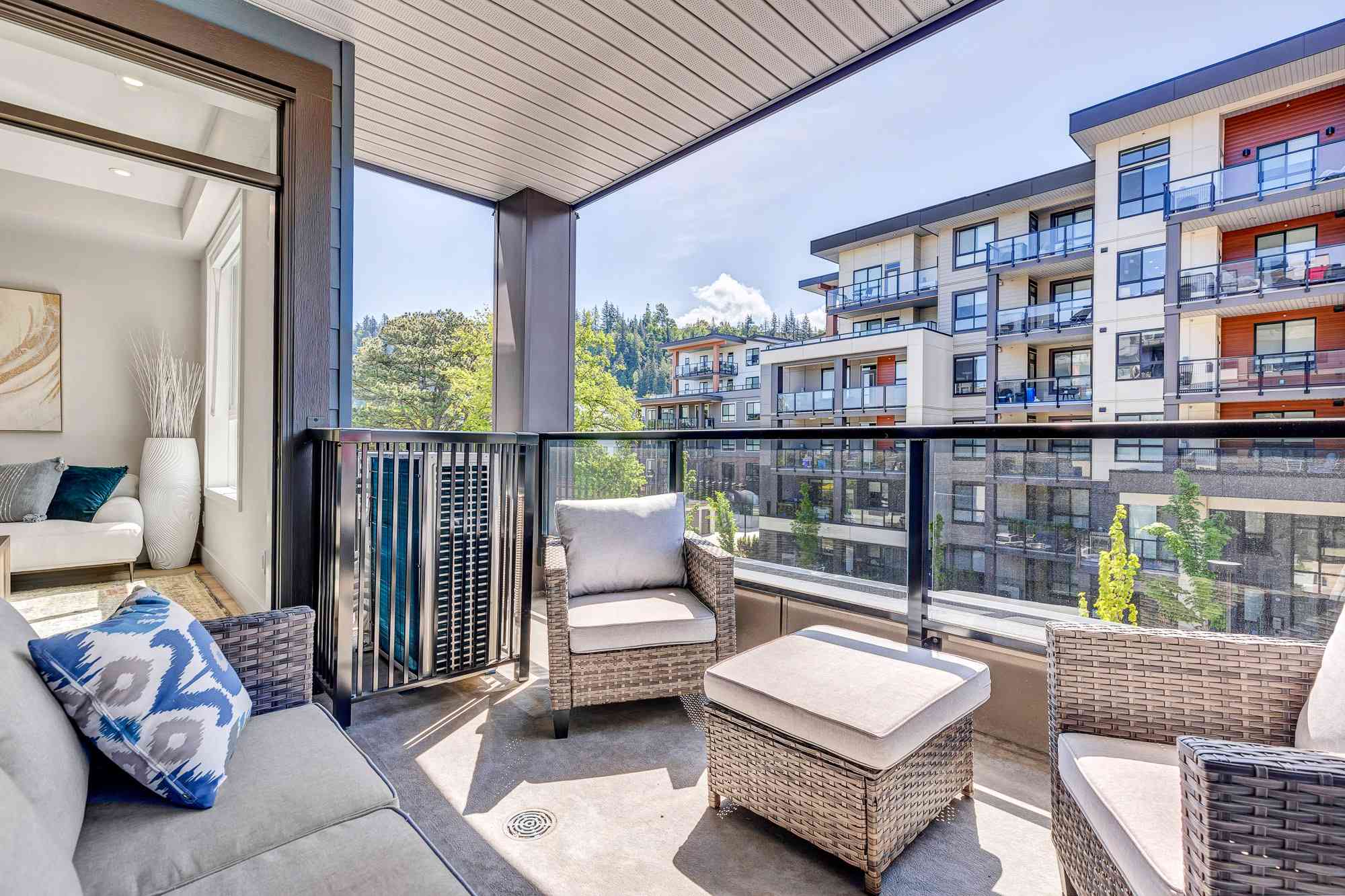 York Residences - Building C – A covered balcony with wicker outdoor furniture, looking out over neighbouring condo buildings and tree-covered hills.