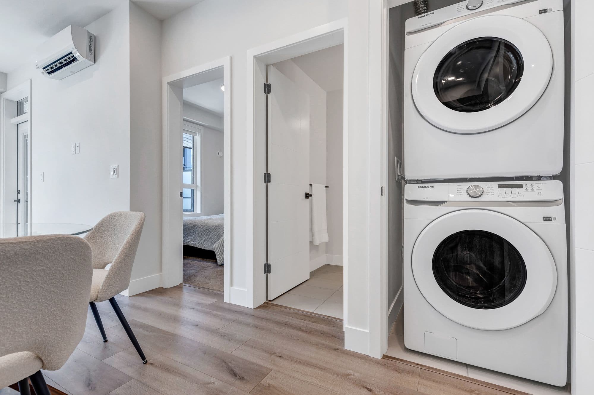 York Residences - Building C – A hallway with a stacked Samsung washer and dryer, wall-mounted air conditioner, and views into a bedroom and bathroom through open doors.