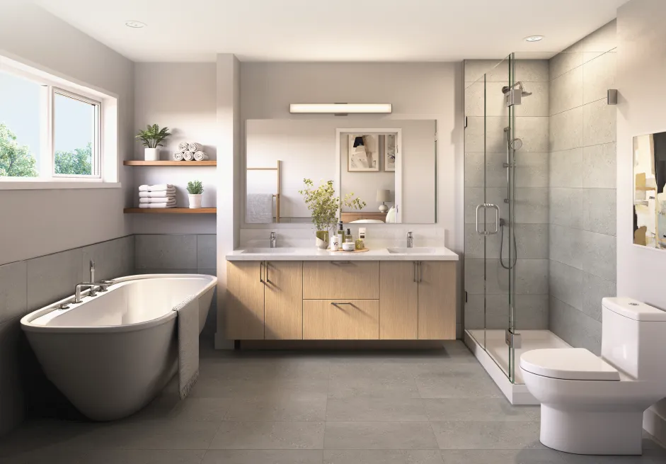 Wildwood Ladner – A modern bathroom featuring a standalone soaking tub under a window, a double vanity with light wood cabinetry, and a frameless glass-enclosed shower. Gray tiled floors and walls create a bright, clean, and spa-like atmosphere illuminated by soft daylight.