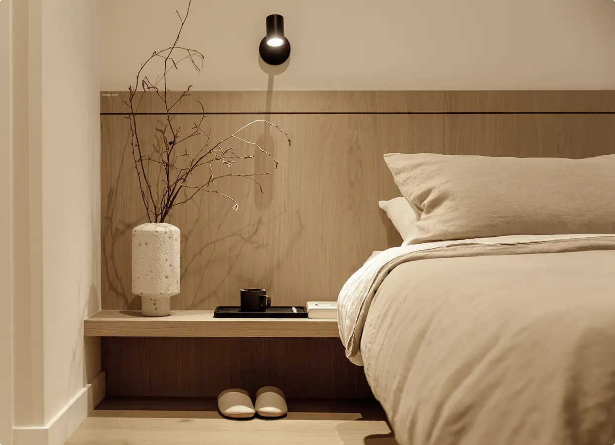 Söenhaus – Close-up of a bedroom nightstand built into a wood headboard, with a ceramic vase, mug, and wall sconce beside a linen-covered bed.