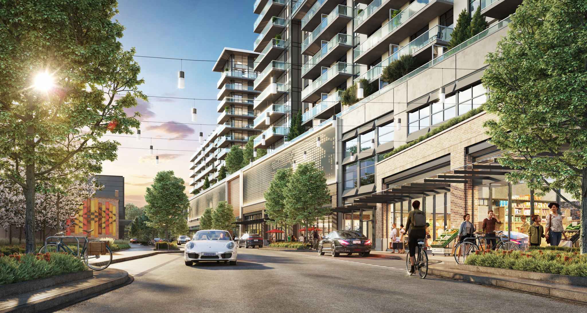 RC at CF Richmond Centre – A ground-level streetscape view of modern residential towers rising above ground-floor retail shops and a grocery store. Pedestrians, cyclists, and luxury cars populate the paved road under strung overhead lights, set against leafy trees and late afternoon sunlight.