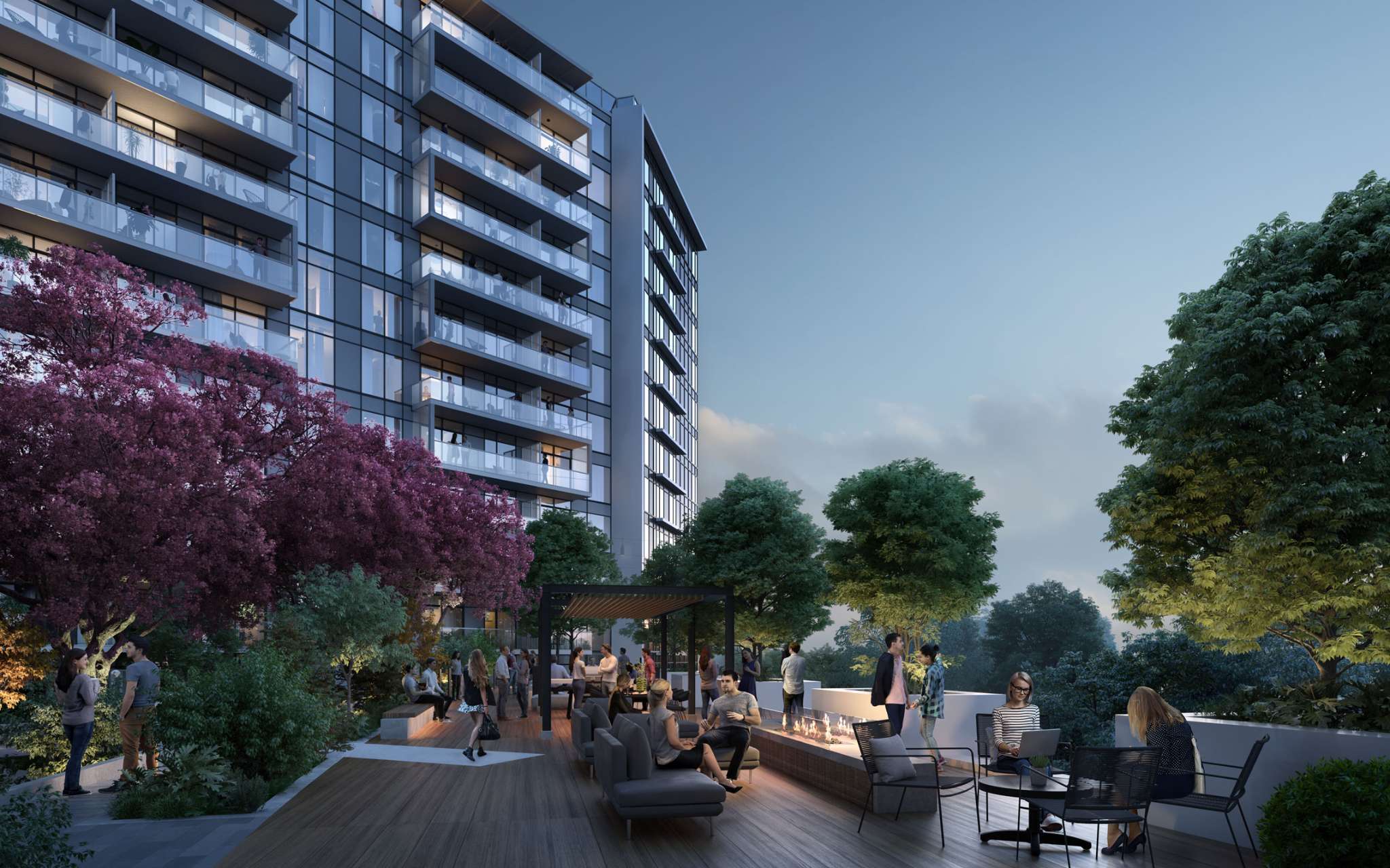 RC at CF Richmond Centre – An outdoor residential terrace features a wooden deck populated with lounge seating, an elongated fire pit, a pergola dining area, and several residents socializing under the dusk sky. Lush green trees and vibrant purple cherry blossoms surround the patio, set directly beside a modern multi-story glass condominium building.
