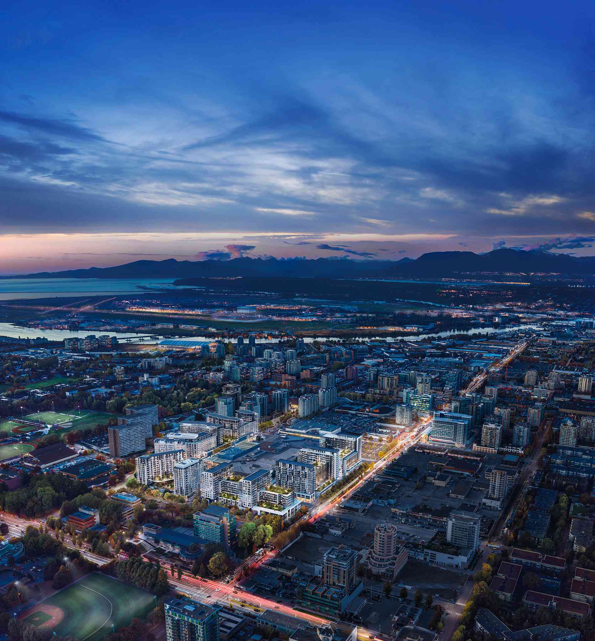 RC at CF Richmond Centre – A high-angle aerial view at dusk shows a sprawling illuminated residential master-planned community seamlessly integrated into a dense urban grid. In the background, a wide river, coastline, and distant mountain silhouettes stretch beneath a dramatic twilight sky.