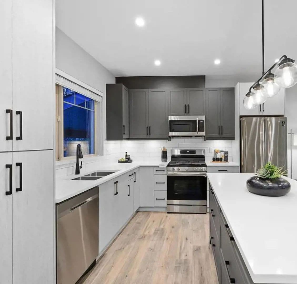 Hillside Homes – Real photo of a kitchen with two-tone gray cabinetry, stainless steel appliances, and a pendant light island.
