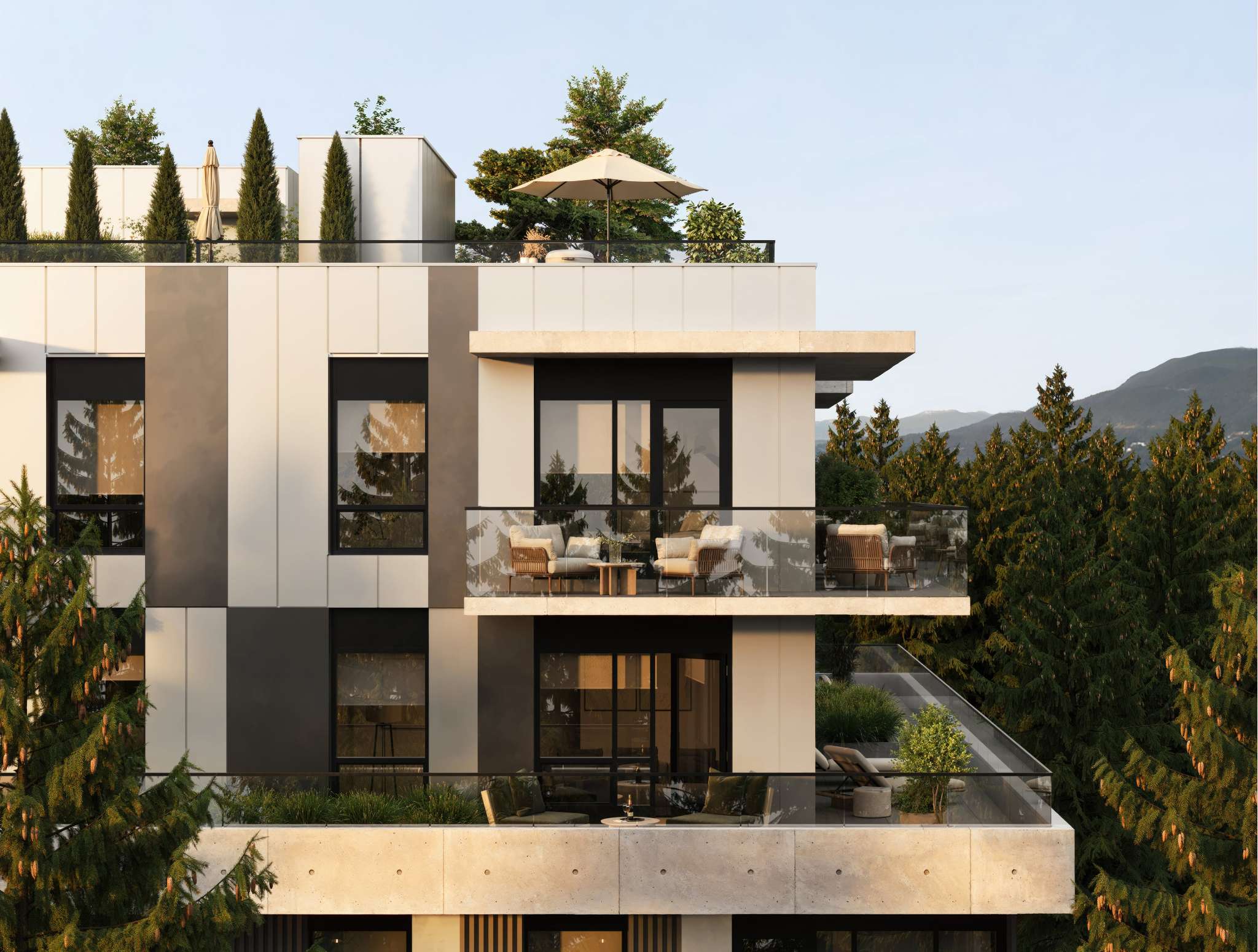 Arden – The upper stories and rooftop terrace of a modern mid-rise building featuring off-white and charcoal paneling, glass railings, and private outdoor seating. Lush evergreen pine trees frame the building, with a distant mountain silhouette visible against a clear, soft daylight sky.