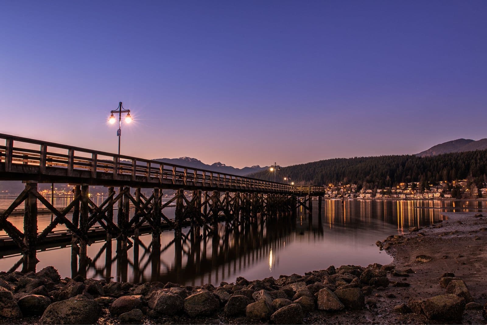 Mary Annes Place – A generic stock photo of a lit wooden pier at dusk over calm water with mountains and town lights in the distance; not clearly tied to the building.