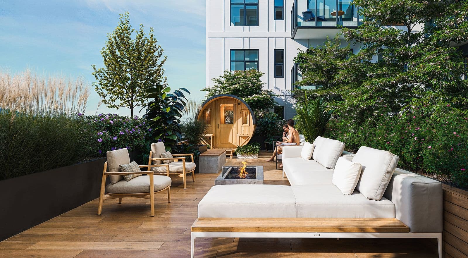 Mary Annes Place – A rooftop terrace with a white outdoor sofa, lounge chairs, a fire pit, and a small wooden sauna surrounded by greenery.