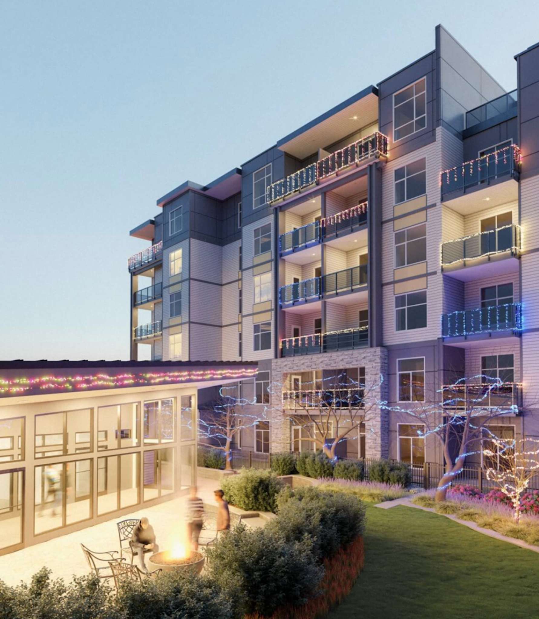 Ledgeview II – A modern multi-story residential building featuring balcony light displays is shown at dusk next to a landscaped outdoor lounge with a fire pit. The ground-level patio includes seating, surrounding greenery, and glass doors leading into a warmly lit common area building.