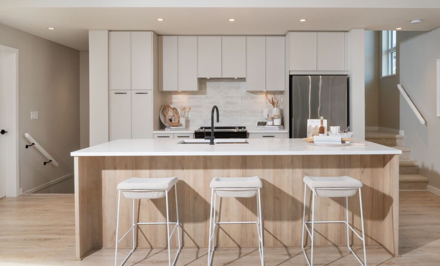 East Ridge – Kitchen with light gray cabinets, a wood island with three bar stools, and a staircase visible in the background.