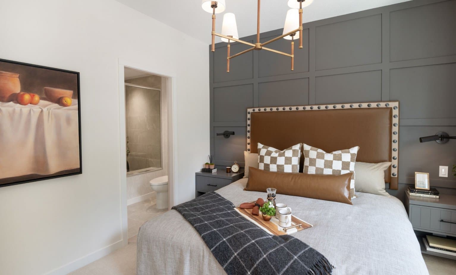 East Ridge – Bedroom with a leather upholstered headboard, dark paneled accent wall, and an ensuite bathroom visible through the doorway.