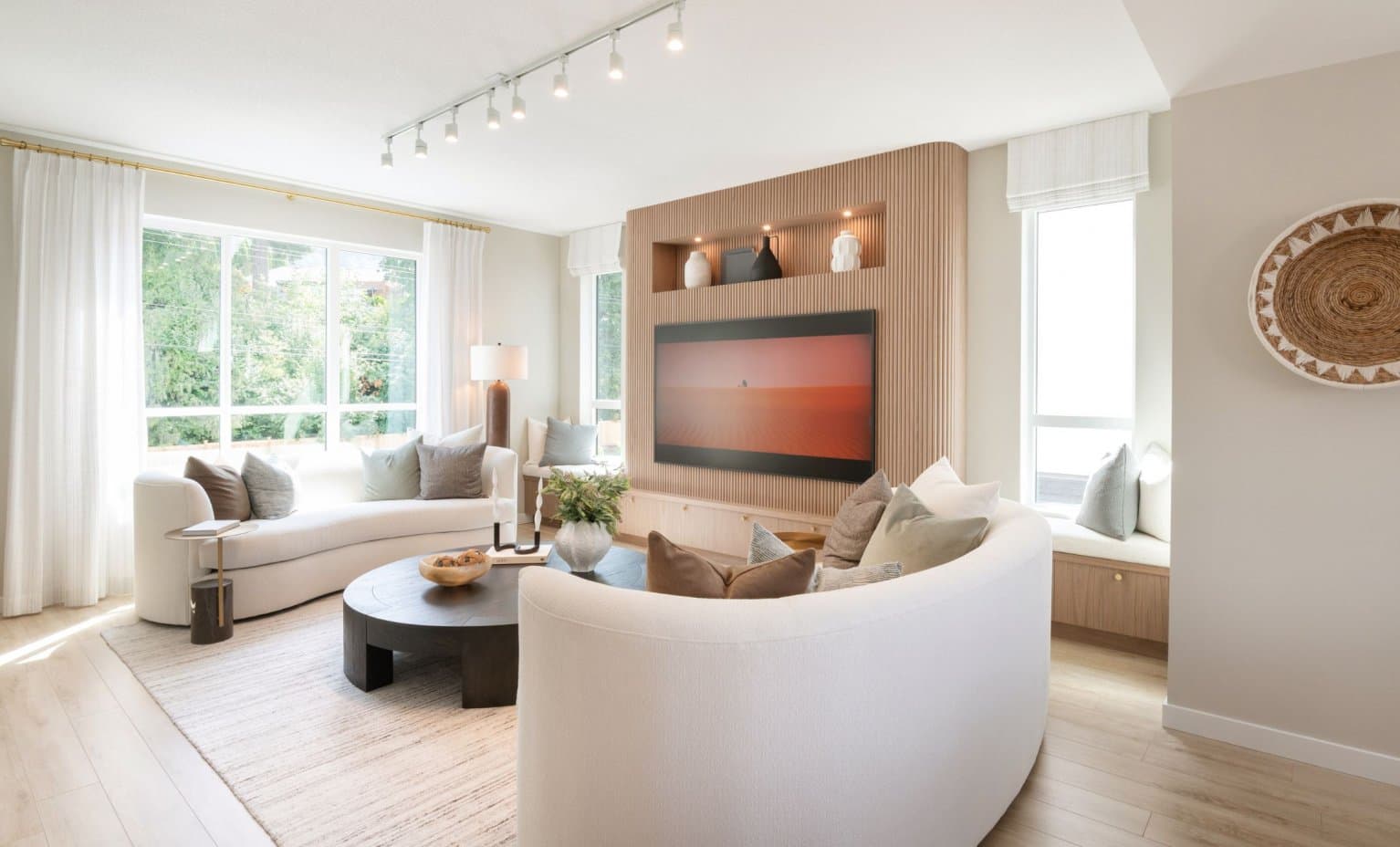 East Ridge – Living room with curved white sofas, a wood-slat feature wall with a mounted TV, and a window seat.