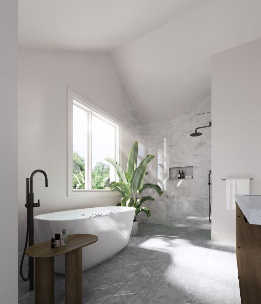 Harlowe House – A bright, modern bathroom featuring a white freestanding soaking tub paired with a matte black floor-mounted faucet, set against grey marble-tiled floors. Natural sunlight streams through a side window onto a lush potted banana plant, with a marble-lined walk-in shower visible in the background under vaulted ceilings.