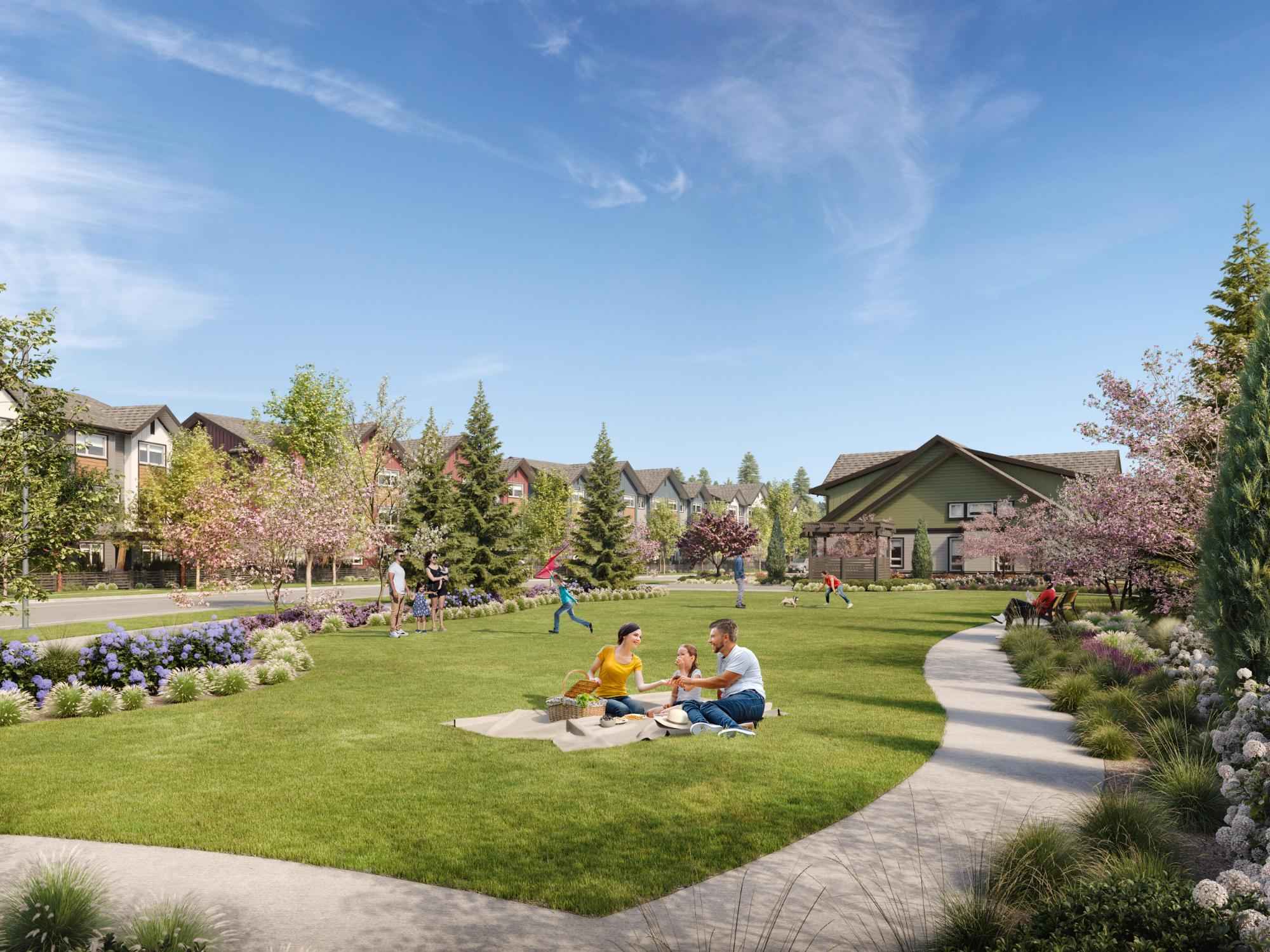 Boardwalk 7 – A spacious outdoor community park and green lawn surrounded by walking paths, blooming flowering trees, and lush landscaping, with residential townhomes in the background. Families and residents are enjoying activities like picnicking, playing, and walking on a bright, sunny day under a blue sky.