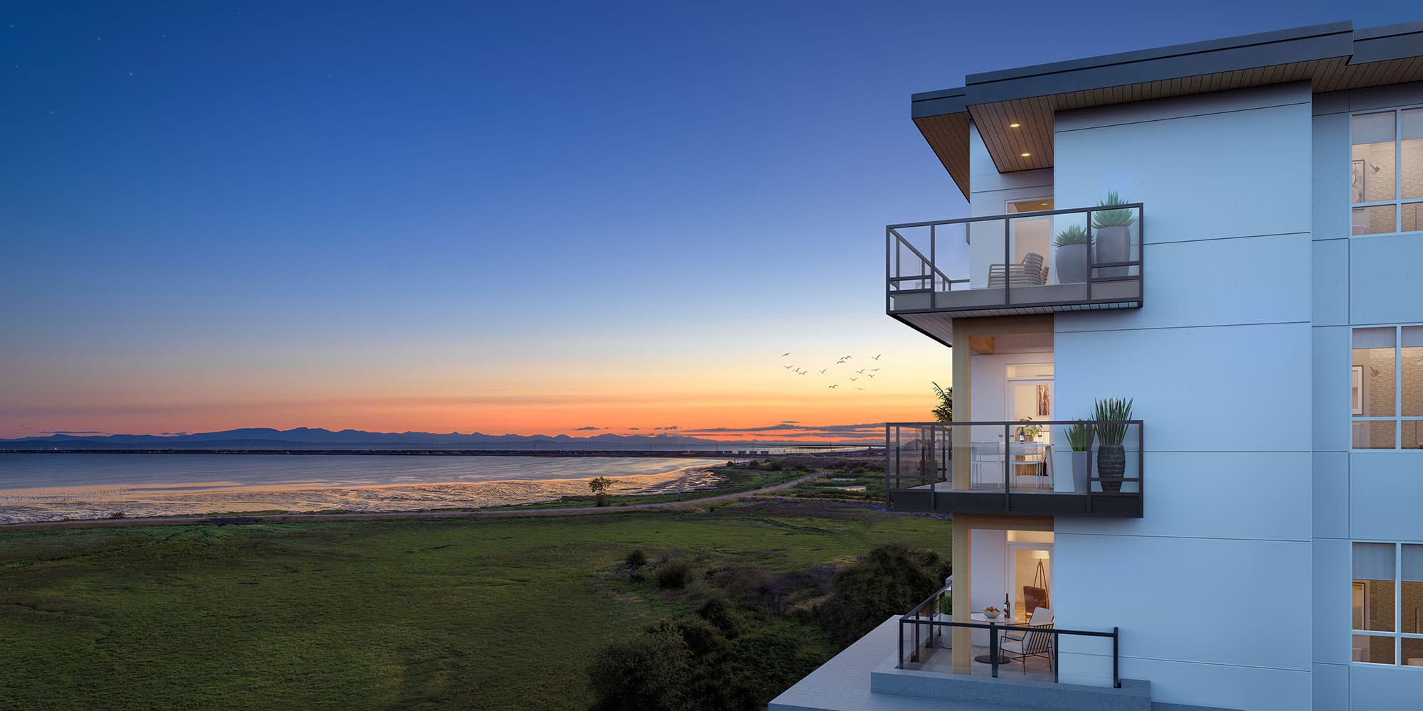 Boardwalk 7 – A perspective looking out from a multi-story residential building's glass-railed balconies across coastal wetlands toward the ocean and distant mountains. The scene is illuminated by a vibrant sunset with a gradient of orange, pink, and deep twilight blue sky above the tranquil water.