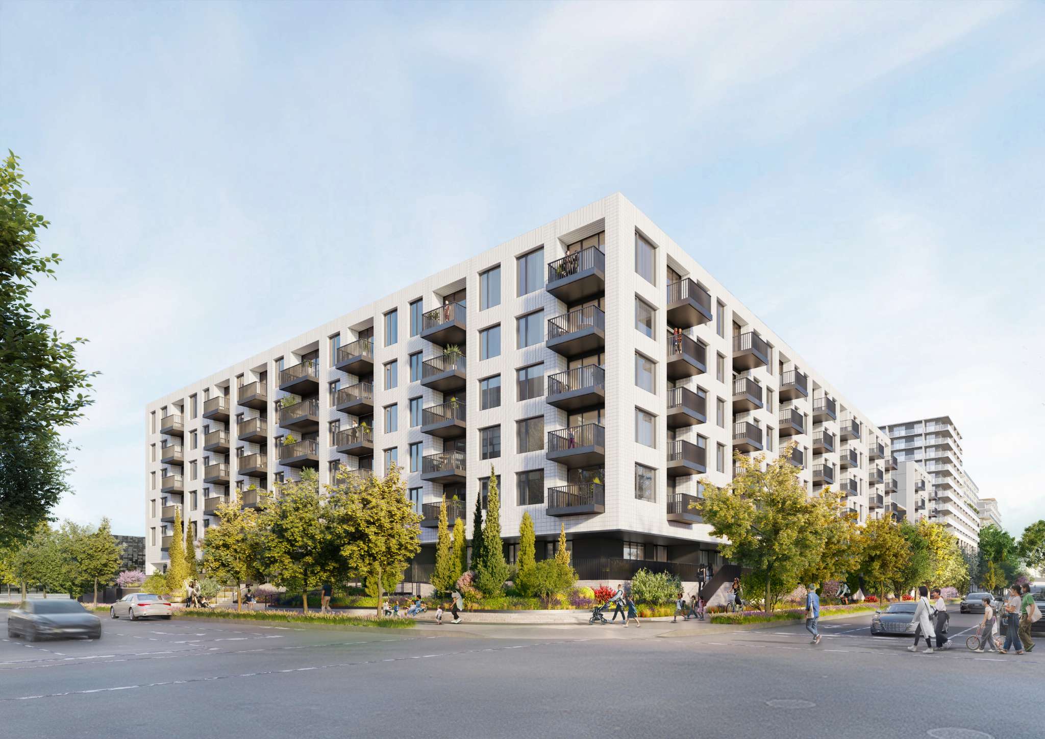 Lansdowne District – A modern, mid-rise residential building clad in white textured brick with dark metal balconies lining its facade under a clear daylight sky. Lush green trees, landscaped gardens, and a paved street filled with pedestrians, cyclists, and cars frame the corner of the development.