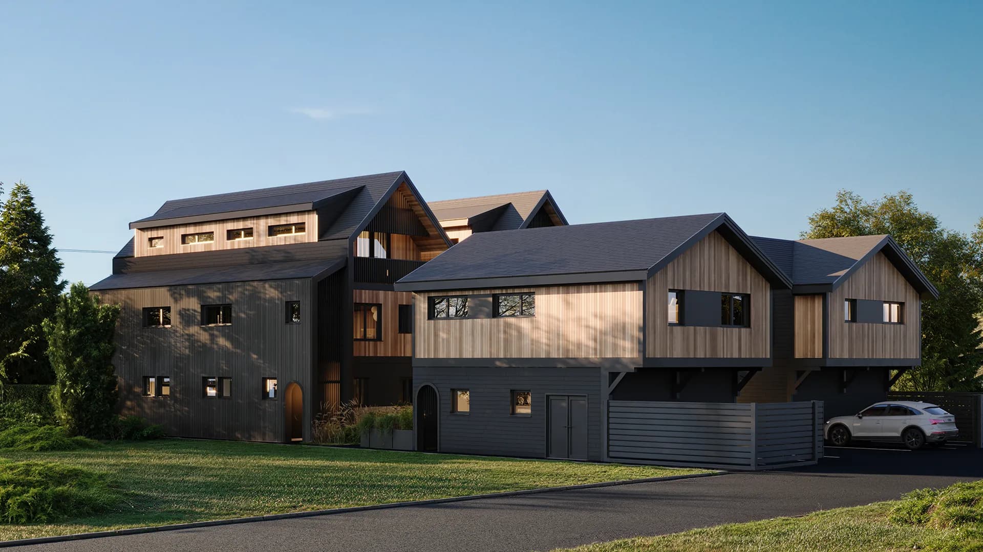 Ansoku – Modern townhome building with dark and wood-tone vertical siding, gabled rooflines, and a landscaped front lawn at dusk.