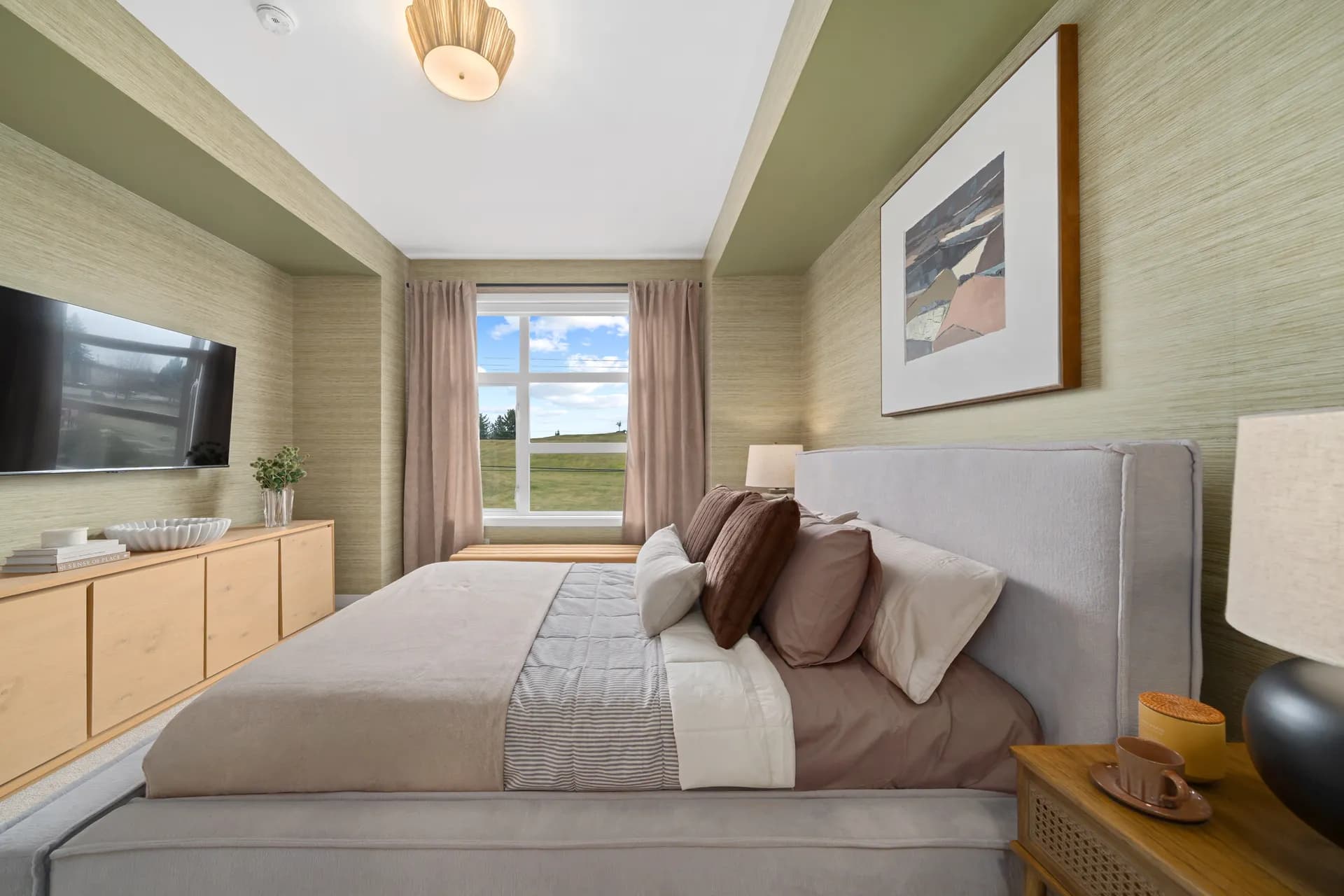 Madison Townhomes – Bedroom with olive green textured wallpaper, a wall-mounted TV, a wood credenza, and a bed with brown and cream bedding.