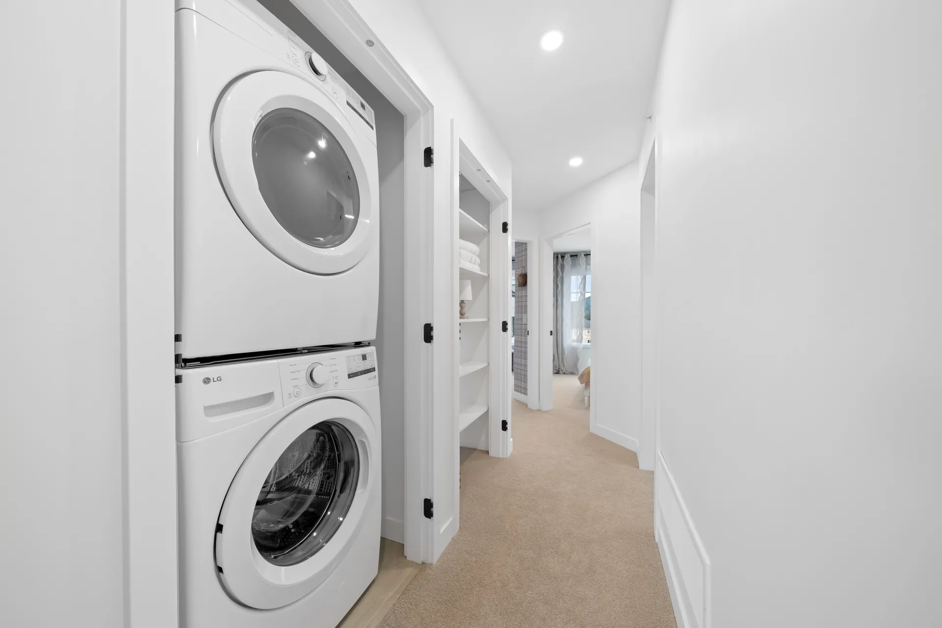 Madison Townhomes – Hallway with a stacked washer and dryer in a closet, leading past a linen shelf toward a bedroom.