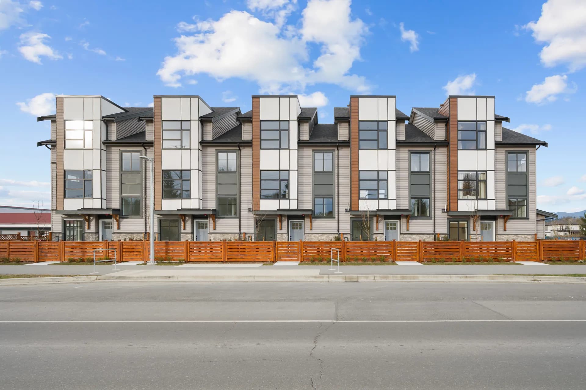 Madison Townhomes – Street-level front view of the townhome row with individual entries, wood fencing, and a clear blue sky.