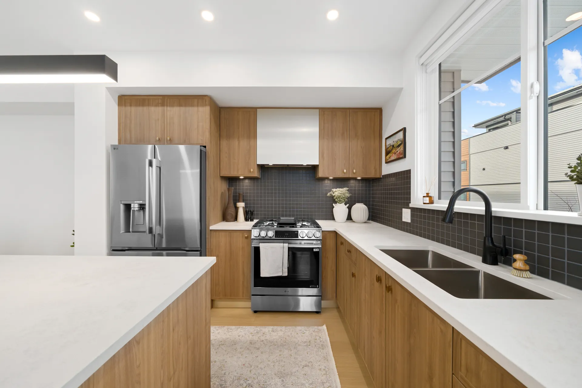 Madison Townhomes – Kitchen with wood cabinetry, a stainless steel range and fridge, dark tile backsplash, and a window looking out to a neighboring building.