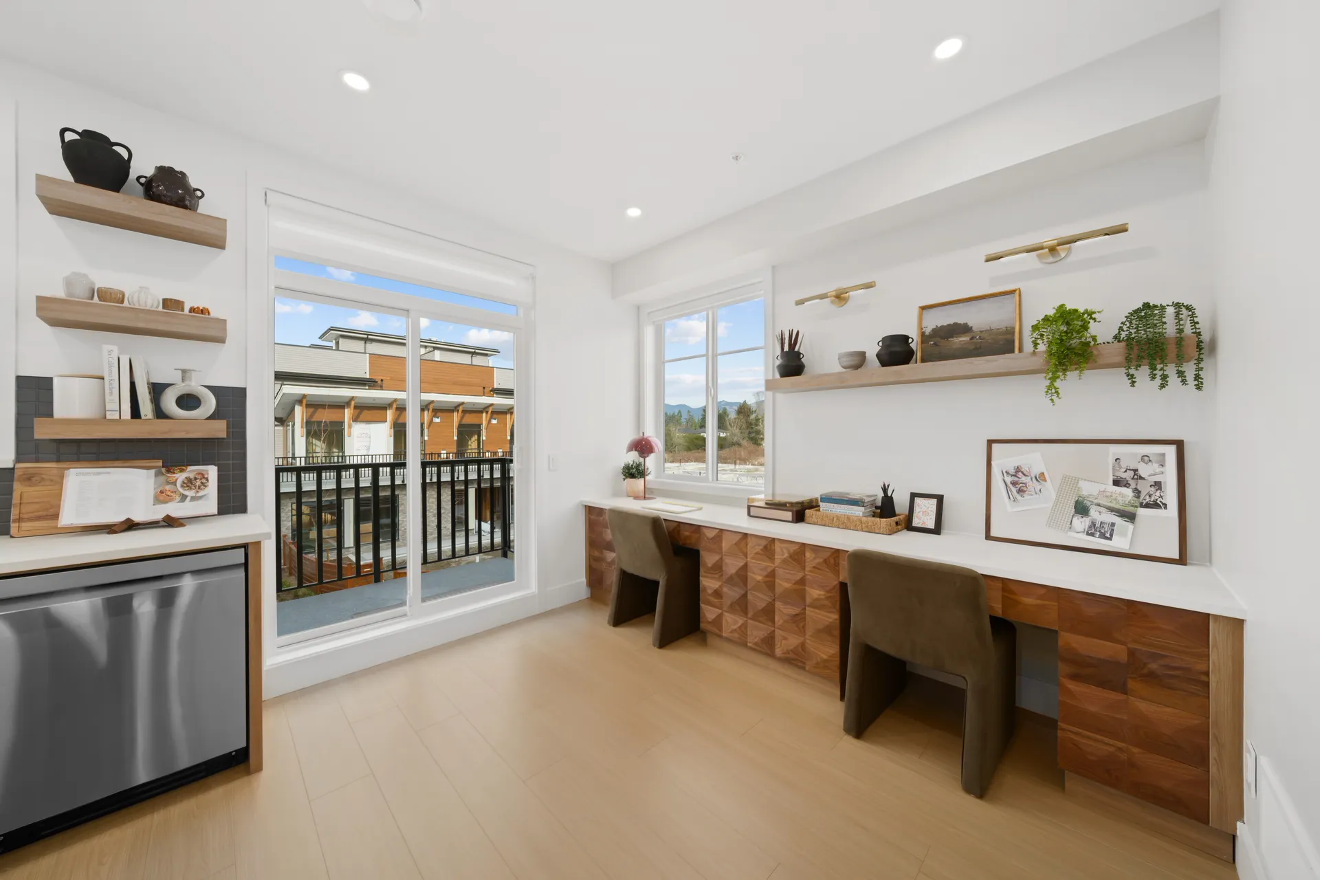 Madison Townhomes – Home office nook with a built-in wood desk, floating shelves with decor, and a sliding glass door to a balcony.