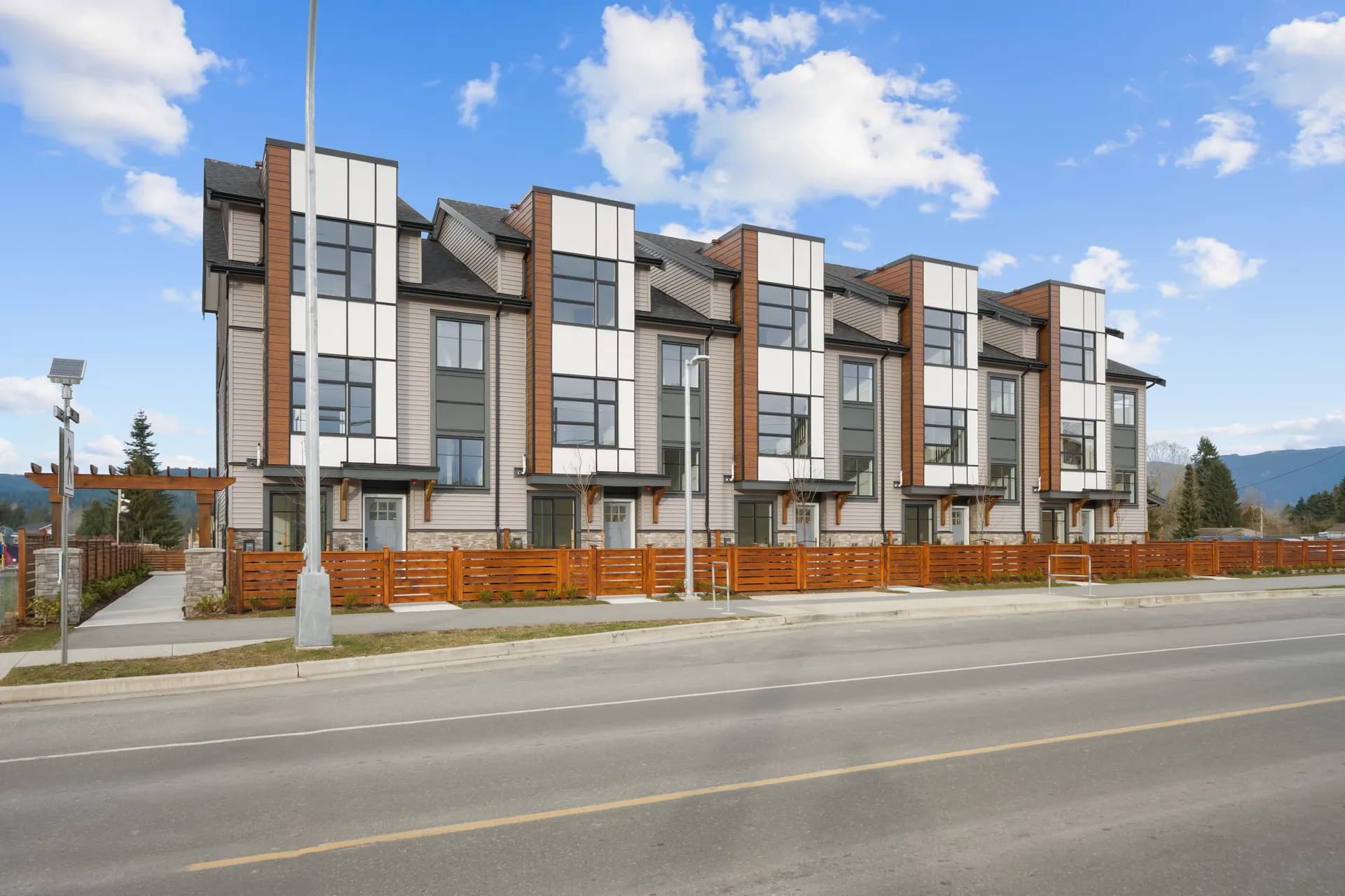 Madison Townhomes – Street-level view of the townhome row's facade with large windows and wood fencing, taken from across the road.