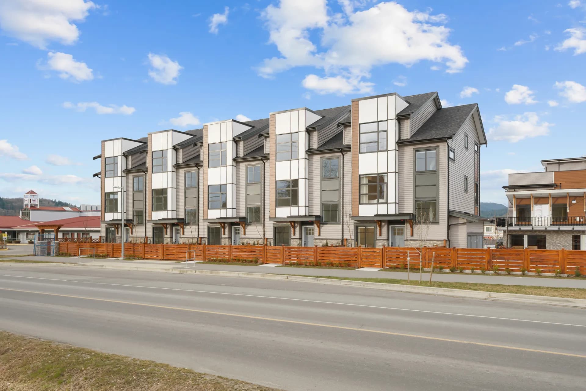 Madison Townhomes – Wider street-level view of the full townhome row with matching gabled rooflines and wood-slat fencing.