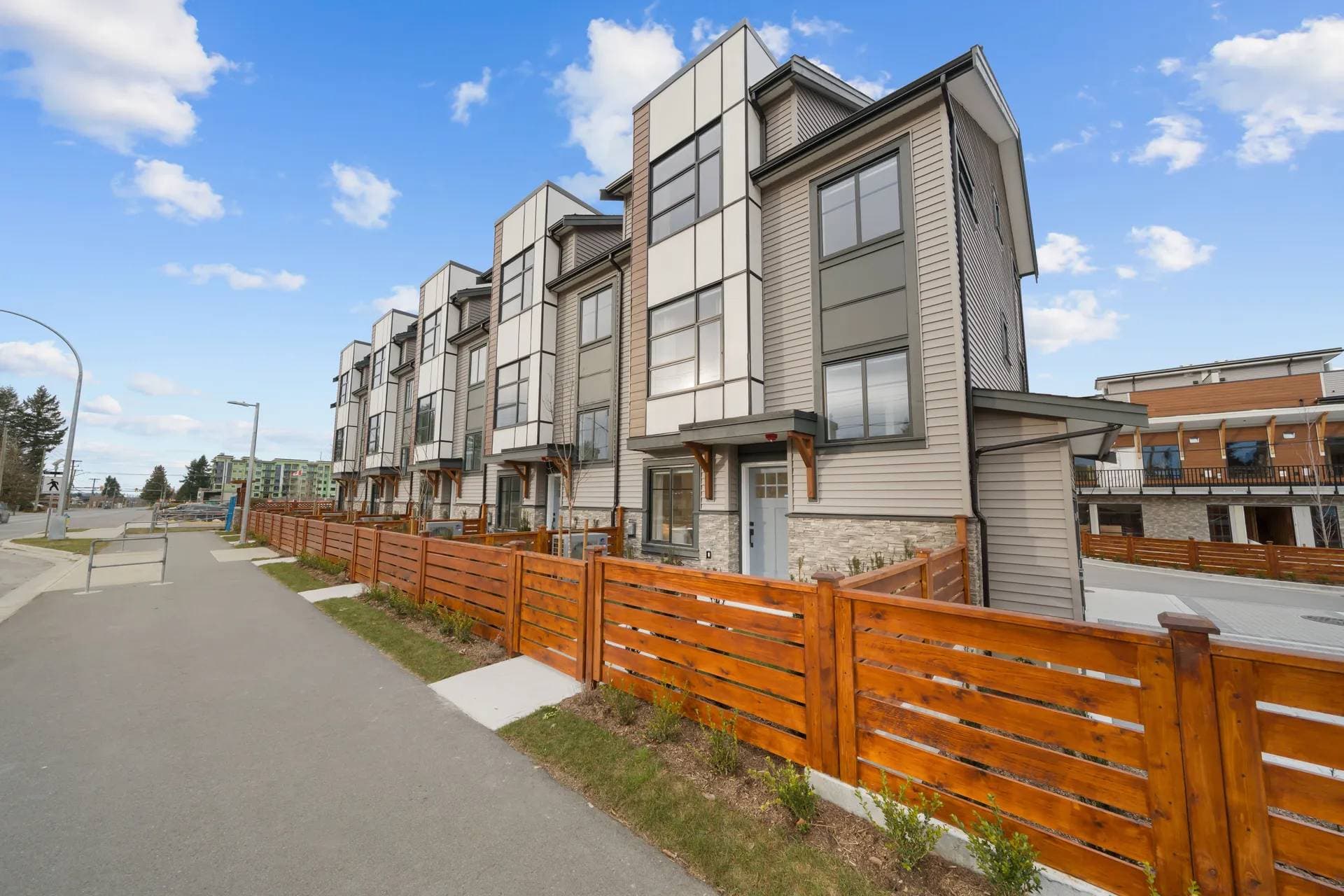 Madison Townhomes – Street-level view of a row of modern townhomes with grey and white siding, wood-toned accents, and a wood fence along the sidewalk.