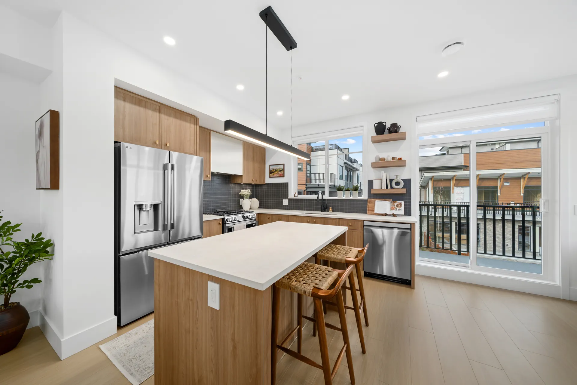 Madison Townhomes – Kitchen with wood cabinetry, a stainless steel fridge, dark tile backsplash, and a sliding glass door leading to a balcony with neighboring townhomes visible.