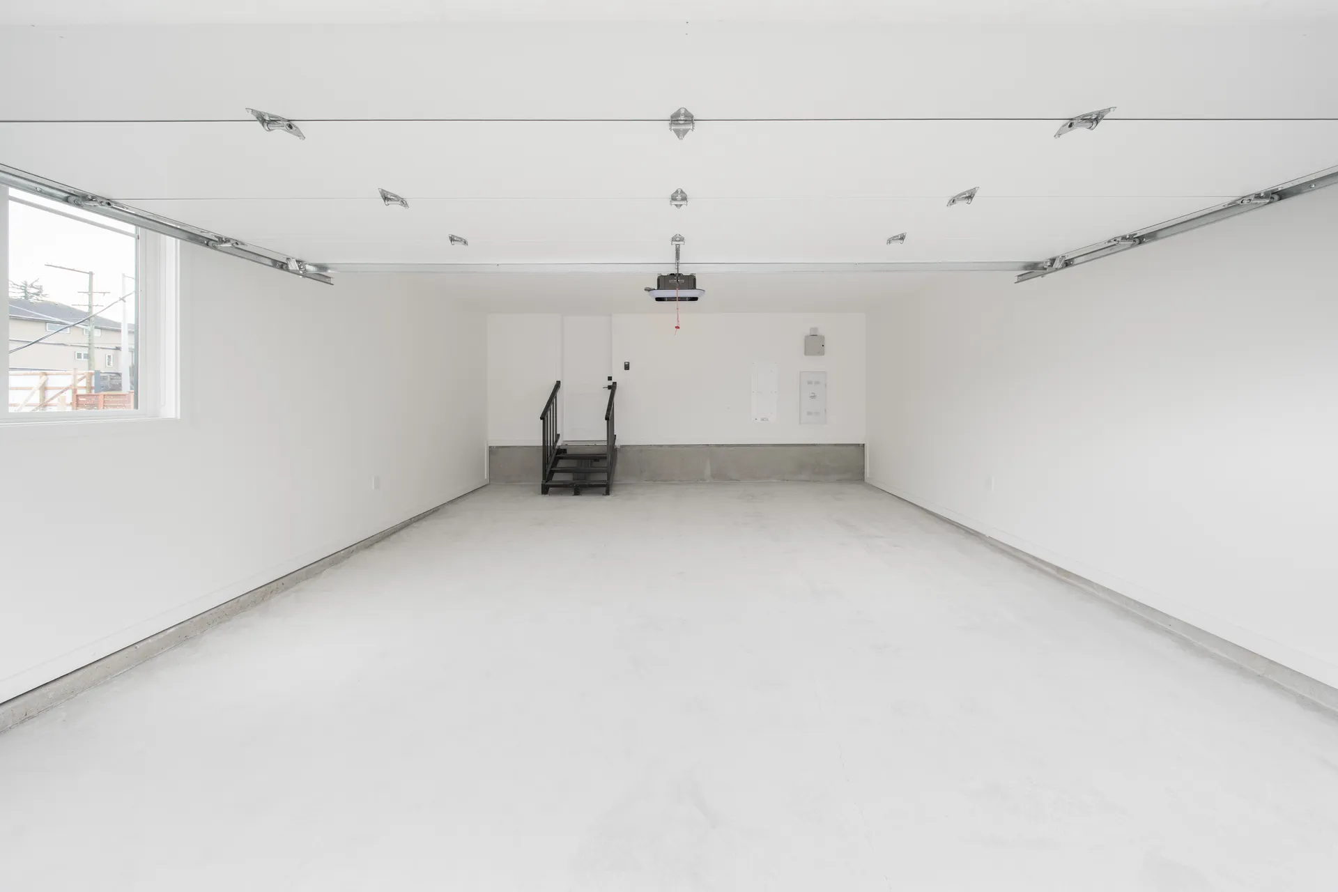 Madison Townhomes – Empty unfinished garage with a garage door, a small staircase, and an electrical panel on the back wall.