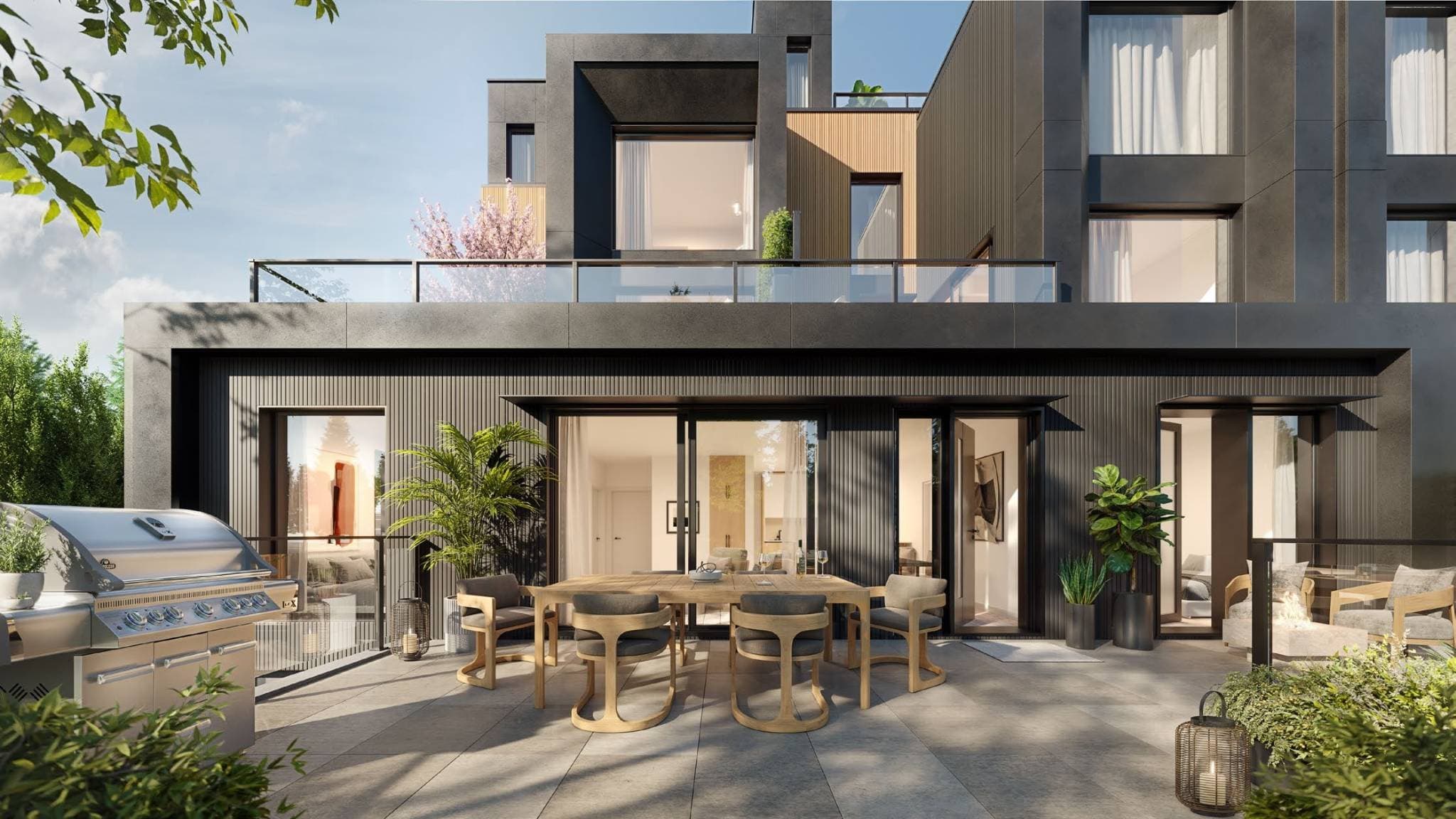 Line House – A bright, sunny terrace outside a modern residential building featuring dark ribbed siding, warm wood accents, and glass-railed balconies above. The patio is furnished with a wooden dining set, stainless steel BBQ grill, and potted greenery, with sliding glass doors looking into the interior.