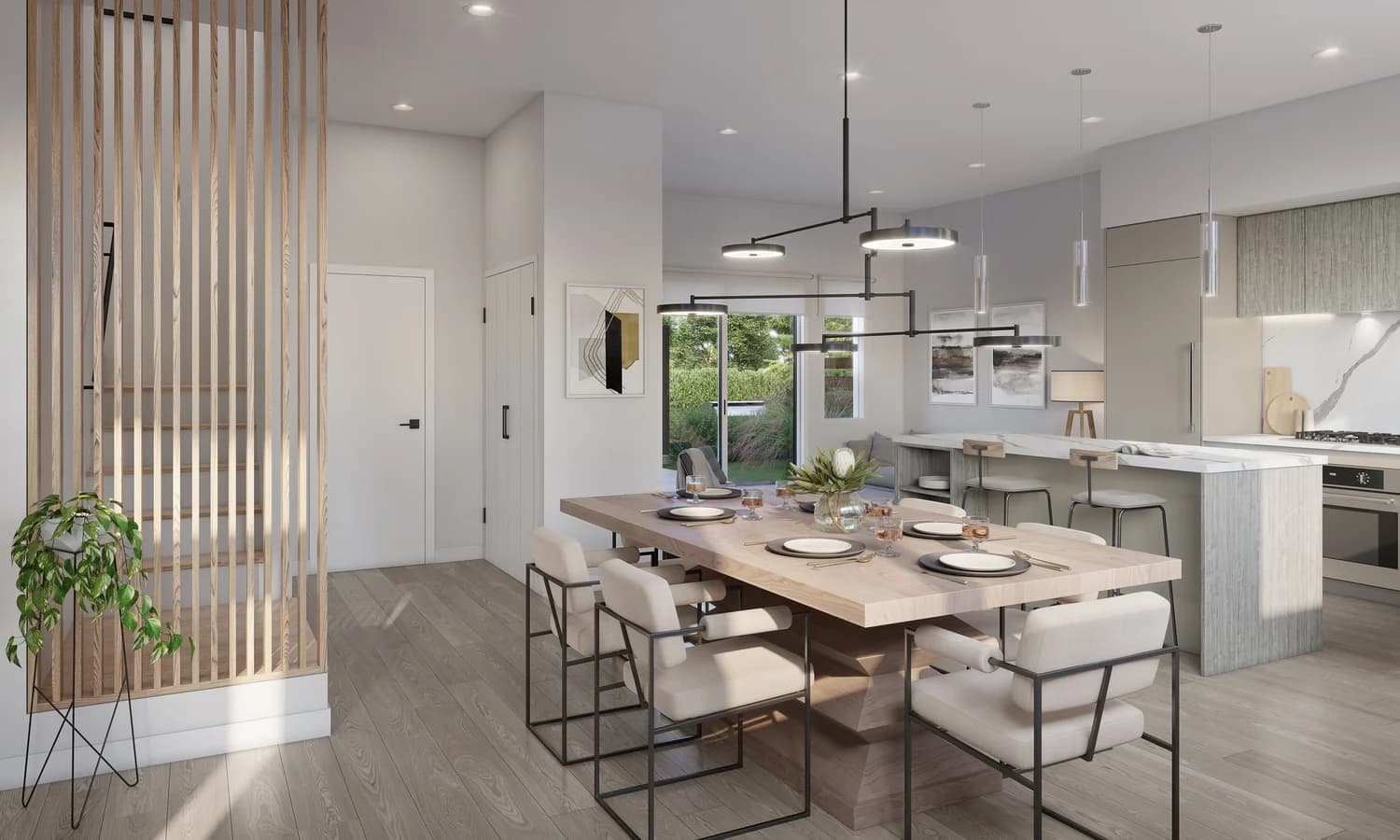 Onward – A bright, open-concept dining room and kitchen featuring a large light wood dining table with contemporary armchairs beneath a black multi-tier pendant fixture. Vertical wood slats frame a staircase to the left, while a marble-topped kitchen island and sliding glass doors leading out to a green yard complete the airy space.