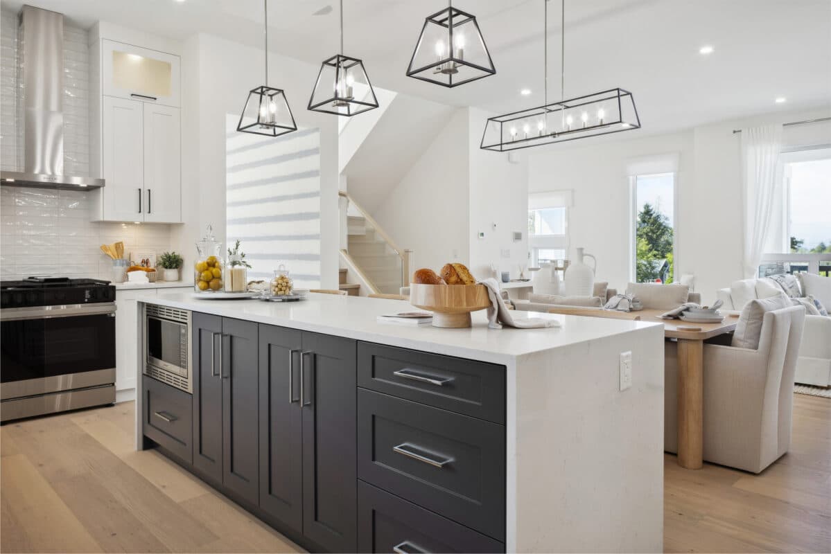 Brookswood Estates – An open-concept kitchen with a dark island, pendant lighting, and a view through to a living room and dining area with large windows.