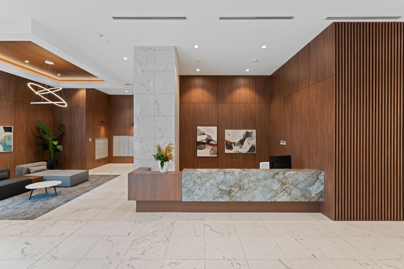 Highpoint Condos – Building lobby with a wood-panelled reception desk topped in blue-grey marble, mailboxes, abstract wall art, and a small seating nook.