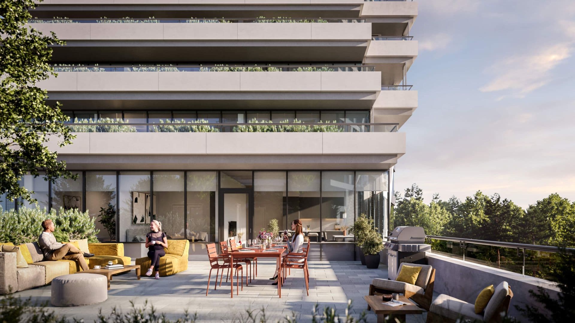 BridgeCity – A spacious outdoor terrace features residents lounging on plush yellow outdoor sofas and dining at a table set for a meal beside a stainless steel barbecue grill. The modern stone patio is situated against the glass façade and stacked concrete balconies of a residential building, overlooking lush green treetops during golden hour.