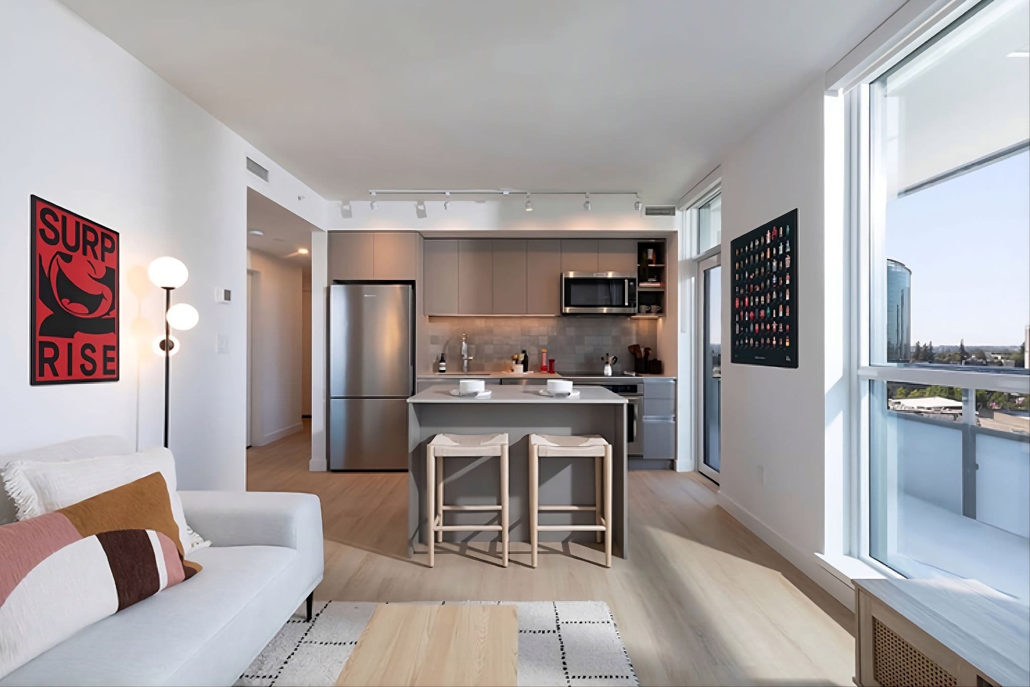 Parkway – Open living room and kitchen with a stainless fridge, island with bar stools, and a balcony door with city view.